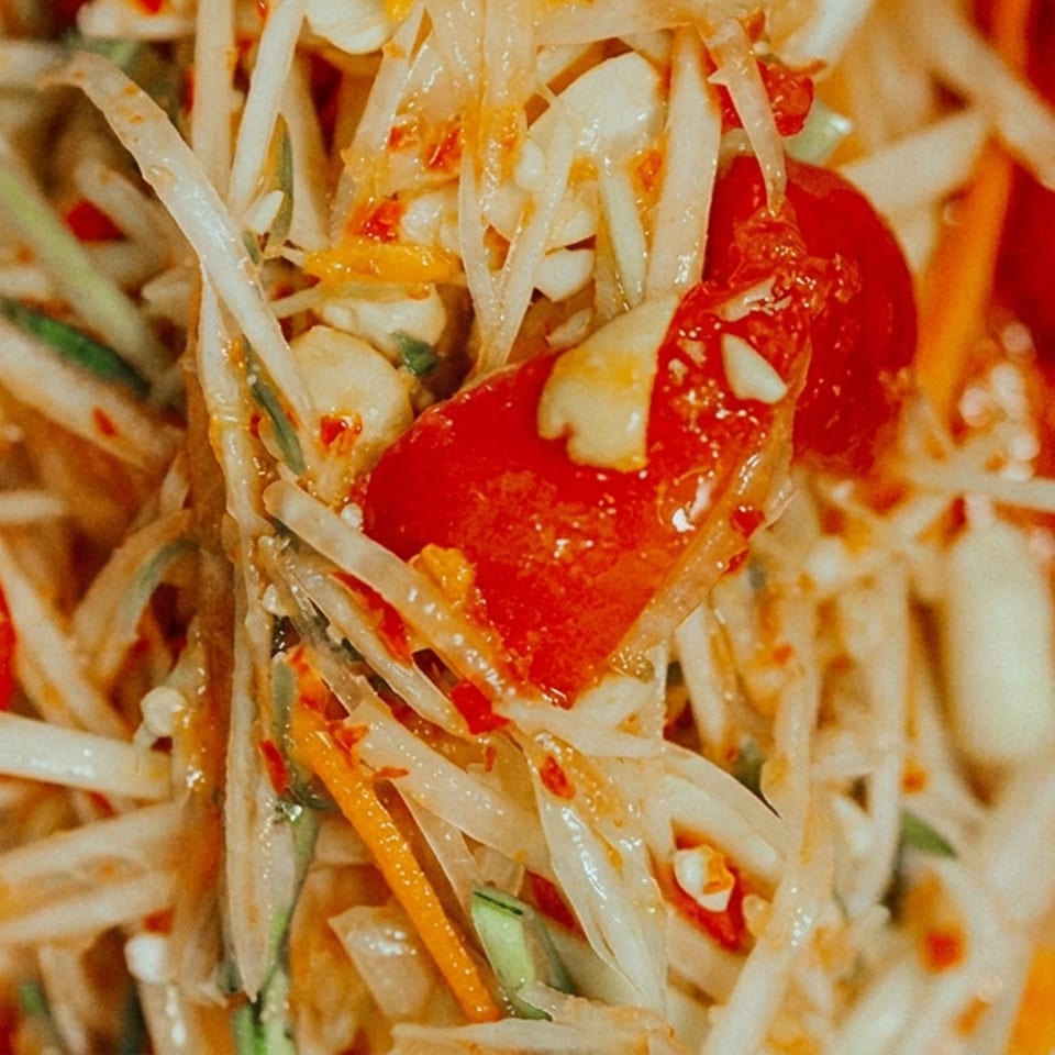 Close-up of spicy Thai green papaya salad with shredded papaya, tomatoes, carrots, green beans, chilies, and peanuts.